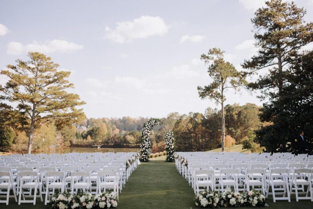 Wide view of outdoor ceremony setup with white chairs and floral arch at TPC Sugarloaf in Duluth Georgia