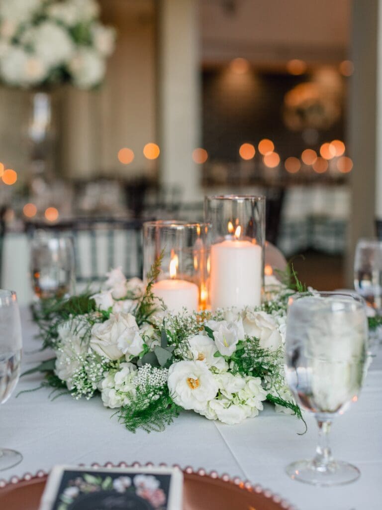 Romantic low wedding centerpiece featuring white flowers and pillar candles for an elegant Sugarloaf Country Club reception.