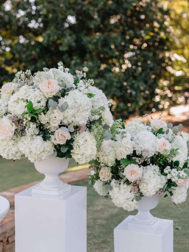 arge white ceremony urn arrangements filled with hydrangeas, roses, and seasonal greenery overlooking the golf course at Sugarloaf Country Club.