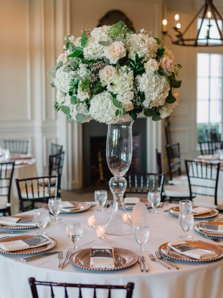 all glass vase centerpiece filled with white hydrangeas, roses, and lush greenery at a Sugarloaf Country Club wedding.