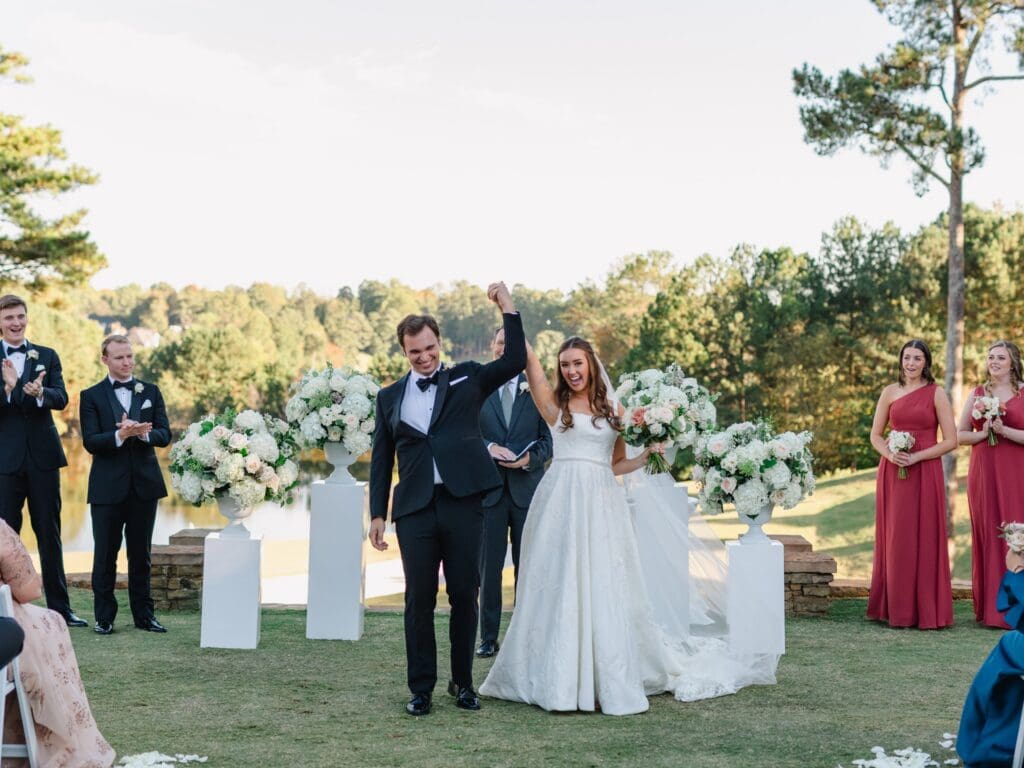 Bride and groom celebrate their ceremony recessional at a Sugarloaf Country Club wedding surrounded by lush white floral urn arrangements overlooking the golf course.