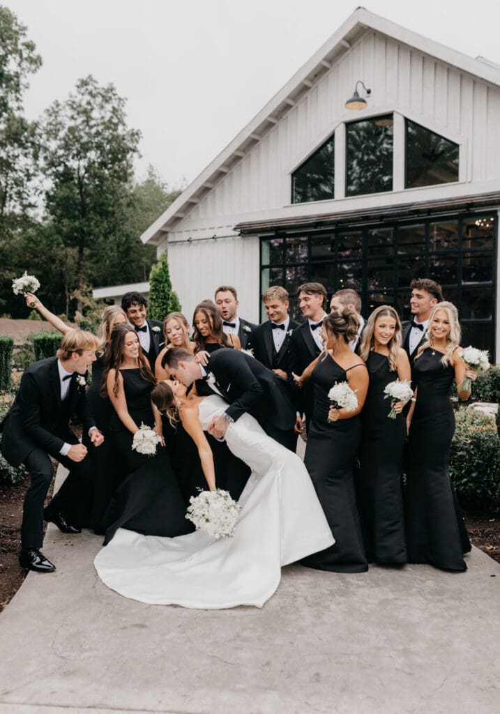 Bridal party in all black tuxes and dresses with white florals at Meadows at Mossy Creek