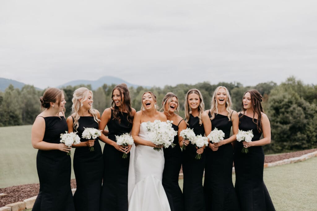 Bridesmaids in black dresses holding white rose bouquets with mountain backdrop at Meadows at Mossy Creek North Georgia