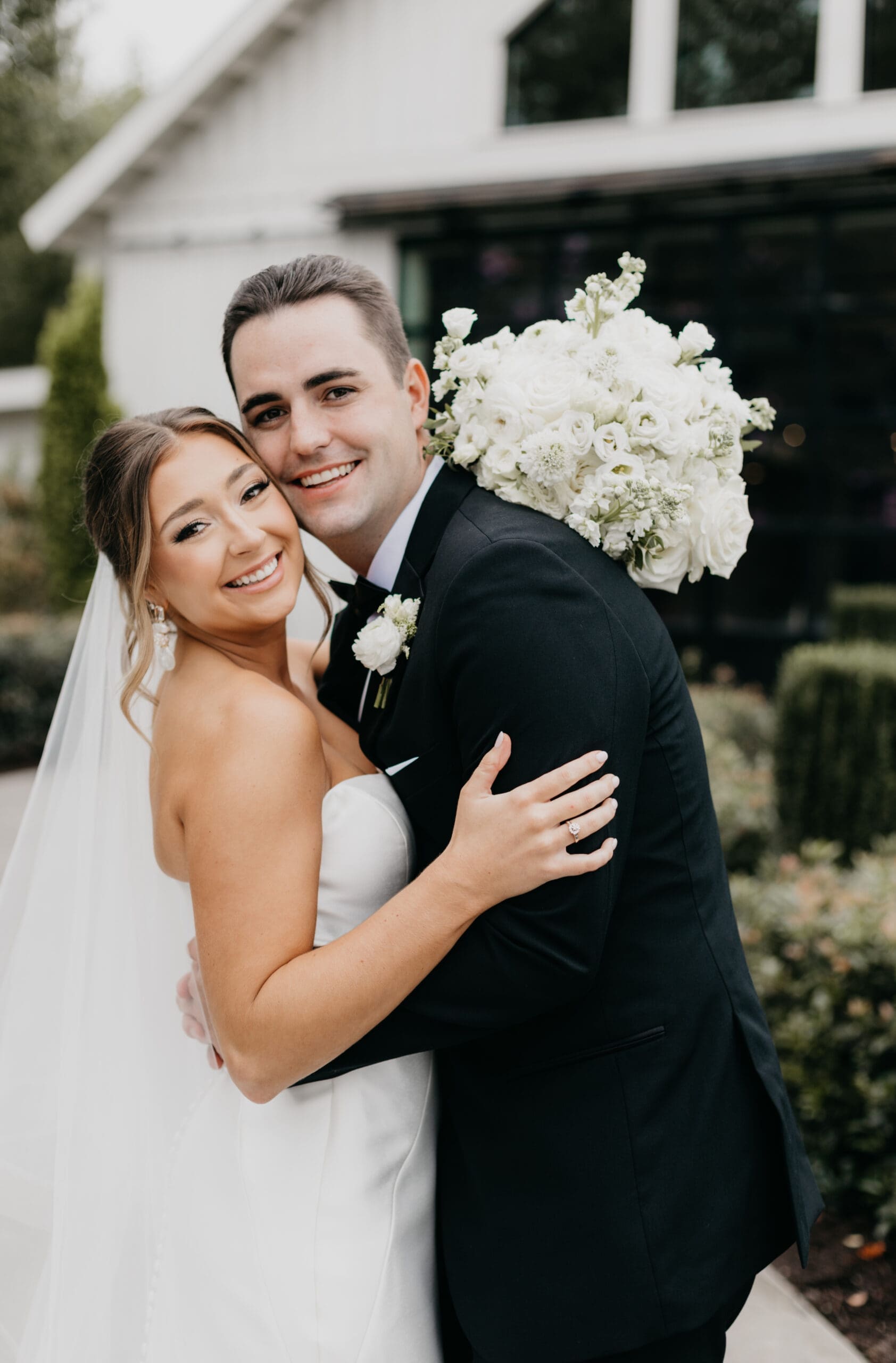 Bride and groom embracing outdoors at Meadows at Mossy Creek with classic all white bridal bouquet by a North Georgia luxury wedding florist