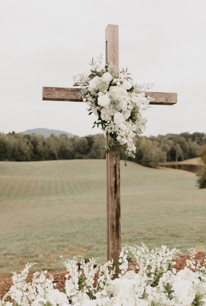 All white floral installation on wooden ceremony cross with mountain backdrop at Meadows at Mossy Creek designed by a North Georgia luxury wedding florist