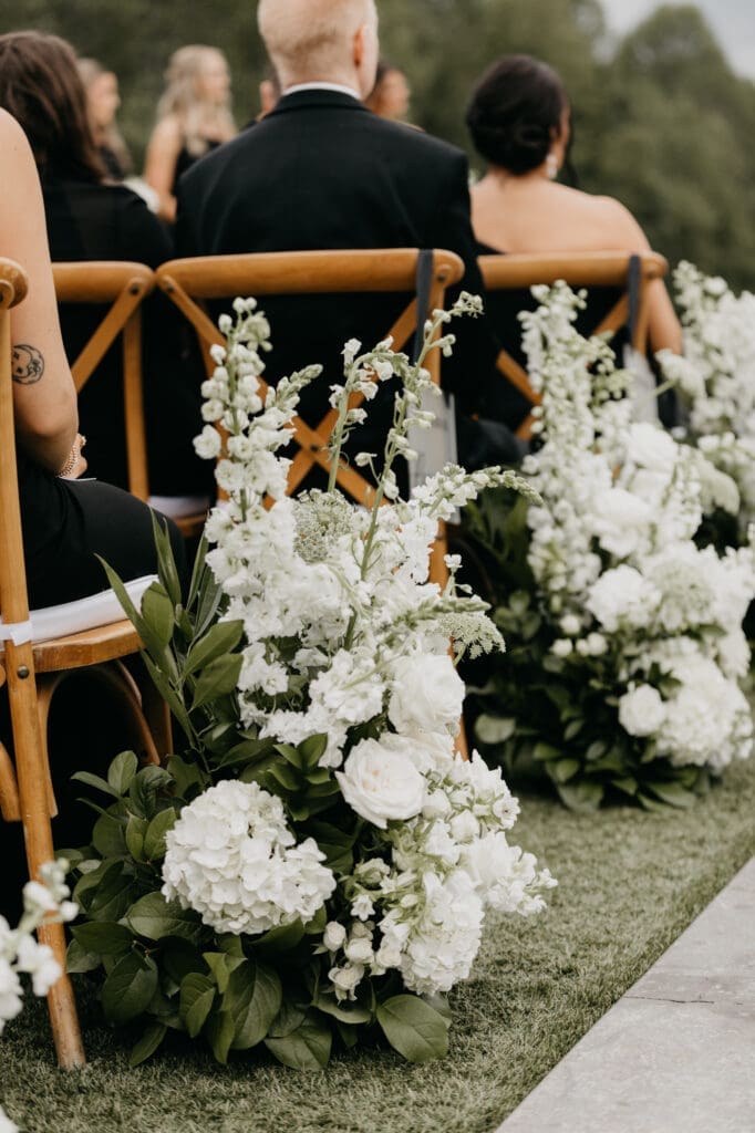 All-white ceremony aisle flowers with hydrangea and rose arrangements lining wooden chairs North Georgia luxury wedding florist