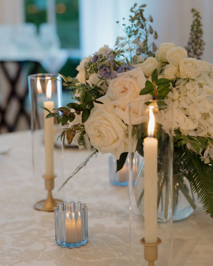 Glass vase with hydrangeas, garden roses and light blue delphinium decorate table at Little River Farms wedding 