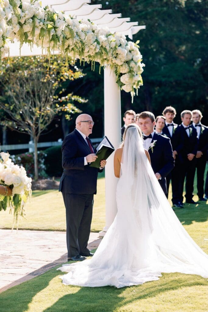 Outdoor wedding ceremony at Greenfield Farm featuring an abundant white floral pergola designed by The Cottage Florals & Event Design.