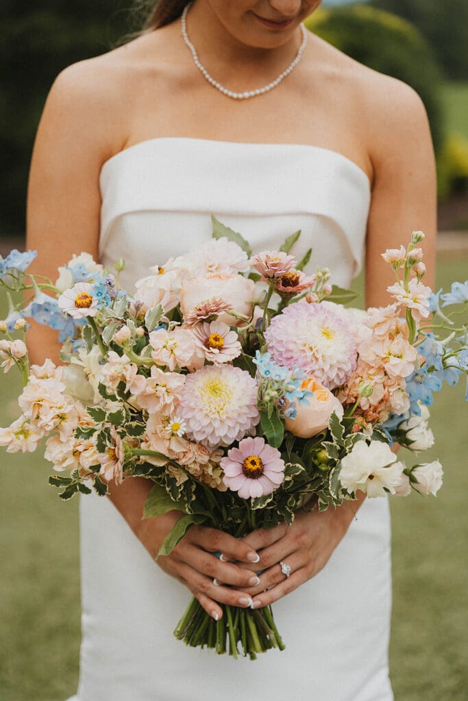 Bride holding pastel garden style bridal bouquet with dahlias, roses, cosmos, and blue delphinium at Meadows at Mossy Creek wedding in North Georgia