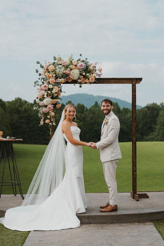 Outdoor ceremony setup at Meadows at Mossy Creek in North Georgia with wooden arbor and pastel garden style wedding florals overlooking mountain views