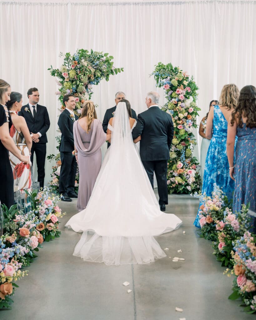 Parents walk bride down the aisle full of colorful blooms at The Revere Wedding Venue