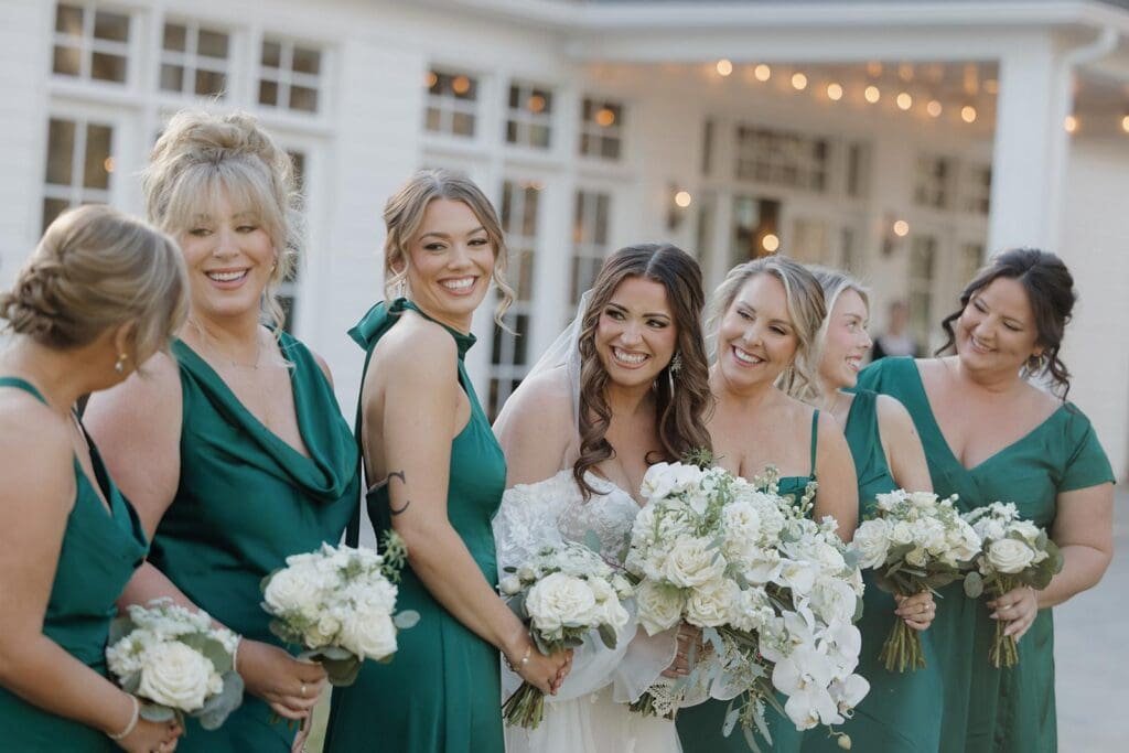 Bridesmaids in emerald green dresses holding white rose wedding bouquets