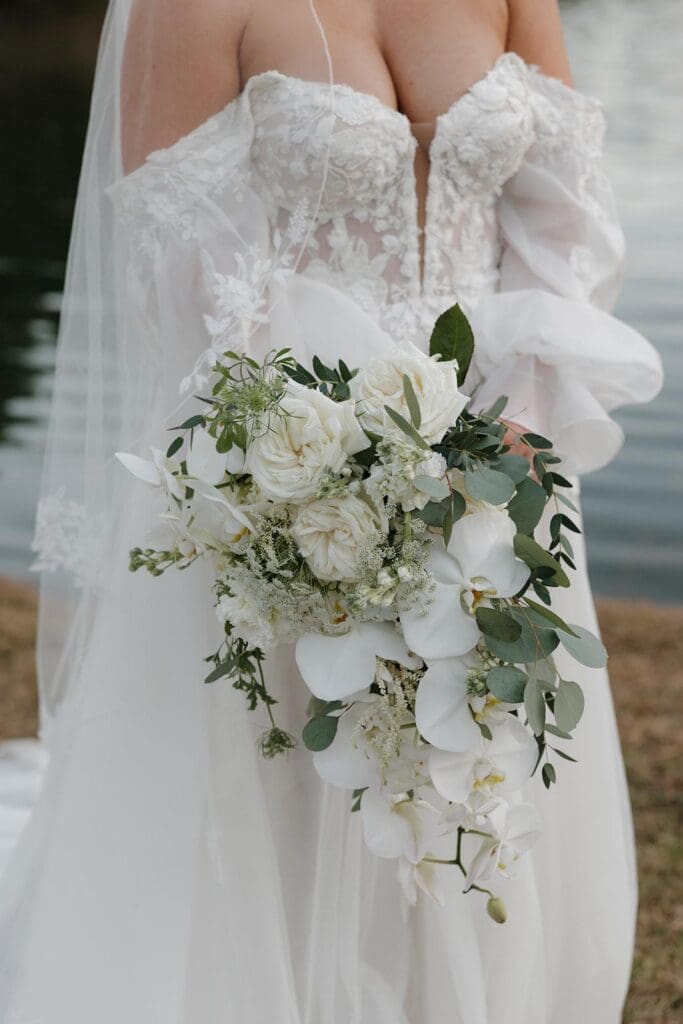 Bridal portrait beside the lake holding cascading orchid bouquet at Little River Farms