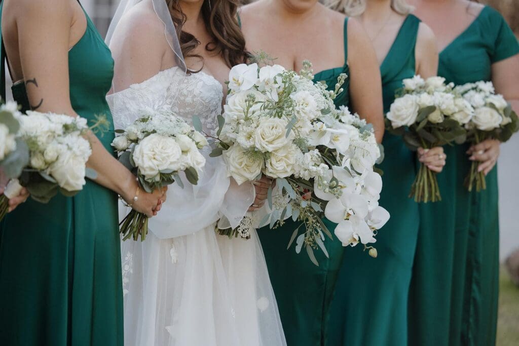 Floral details of Bridesmaids in emerald green dresses holding white rose wedding bouquets