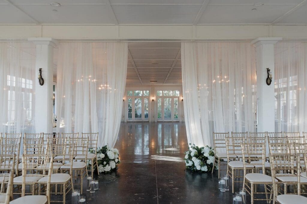 Indoor wedding ceremony aisle with white drapery and floral arrangements at Little River Farms North Georgia