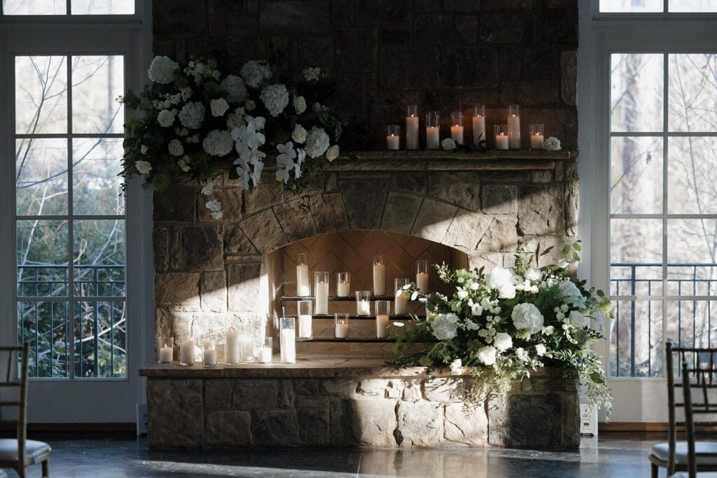 Stone fireplace ceremony backdrop with white hydrangea and rose floral arrangements and pillar candles at Little River Farms wedding