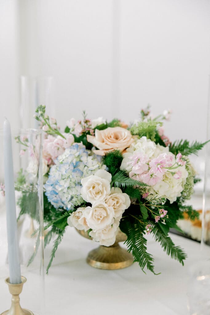 Wedding reception centerpiece with blue hydrangea, ivory roses, and greenery designed for a summer wedding at The Revere.