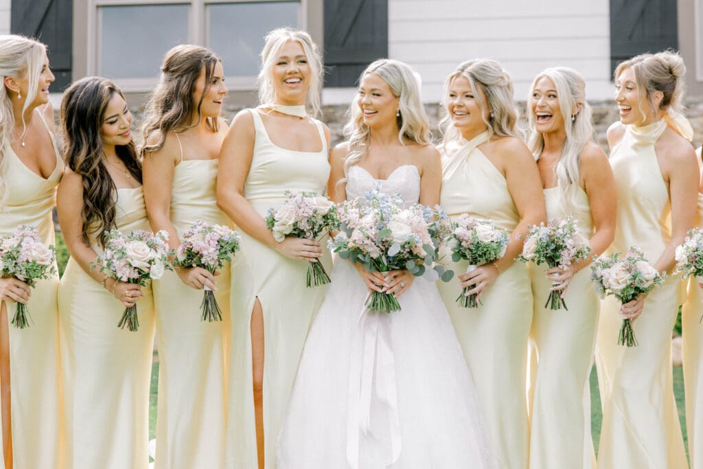Bride with bridesmaids in soft yellow dresses holding pastel garden style bouquets at The Revere wedding venue in North Georgia.