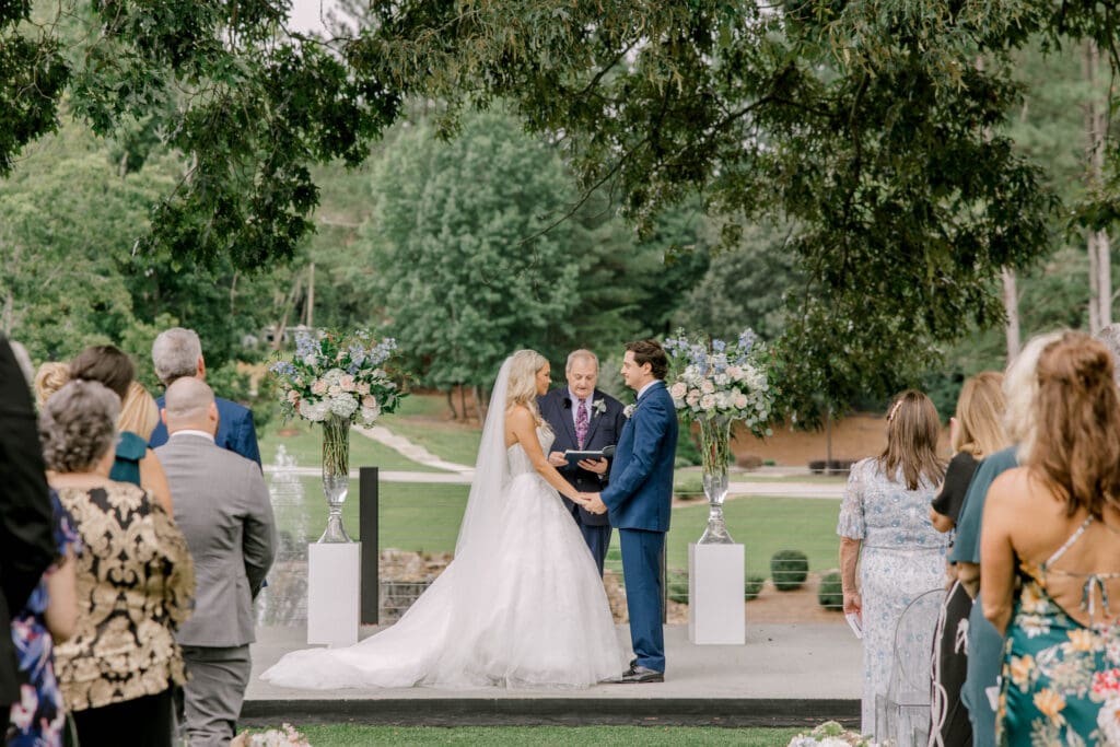 Bride and groom exchanging vows during an outdoor wedding ceremony at The Revere in Dawsonville Georgia.