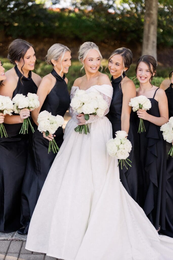 Bride with bridesmaids in black dresses holding white rose bouquets at TPC Sugarloaf wedding