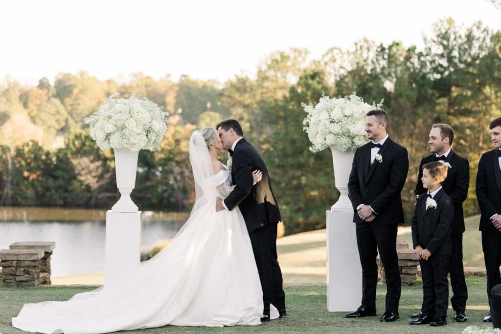 Bride and groom first kiss at TPC Sugarloaf wedding ceremony with white floral urn arrangements