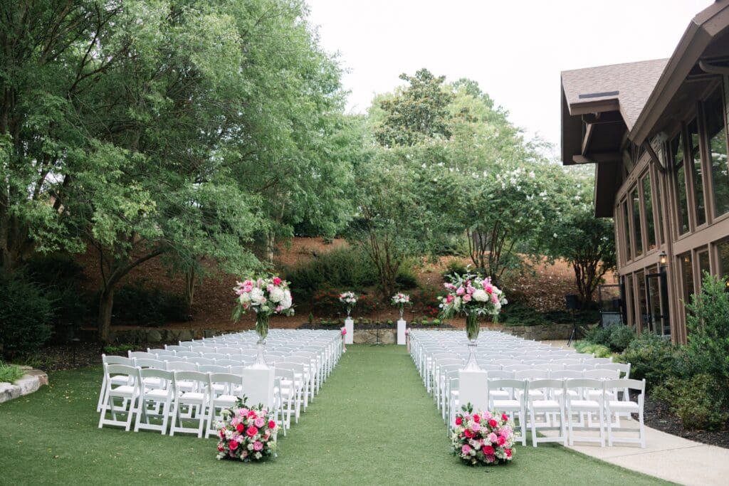 Outdoor wedding ceremony at Country Club of the South featuring elevated pink and white floral arrangements lining the aisle in Johns Creek Georgia.