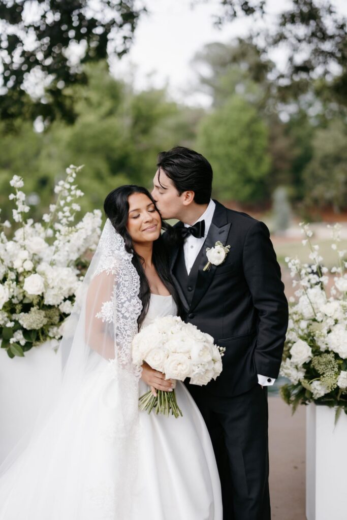 Bride and groom surrounded by garden-style white ceremony flowers on pedestal stands